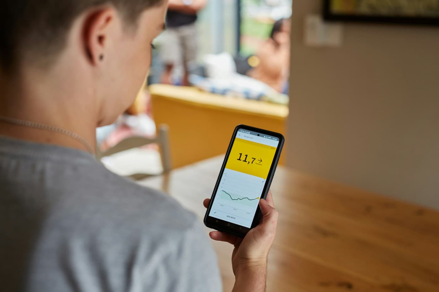 Stock photo: a person at a kitchen table viewing glucose readings on a phone app